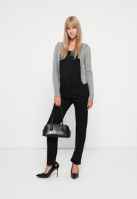 Siva zip-up dukserica, crni top, crne traperice i crne visoke pete. Drži malu crnu torbicu. Jednostavan, elegantan dizajn.