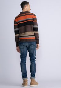 Gebreide trui met horizontale strepen in oranje, zwart, grijs en bruin; hoge nek, geribde manchetten, gecombineerd met blauwe denim jeans en tan laarzen.