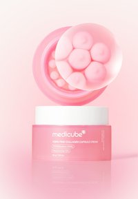 Pink kosmetisk cremekrukke med gennemsigtigt låg, der viser runde kapsler indeni. Emballagen har rene linjer og en etiket, der angiver nøgleingredienser.