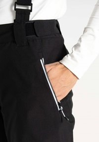 Schwarze Hosen mit einer Reißverschlusstasche, ausgestattet mit einem Riemen und Klettverschluss am Bund. Der Stoff hat ein glattes, strukturiertes Aussehen.