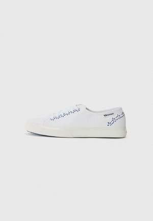 White canvas sneaker with a textured rubber sole, featuring blue floral accents on the side and matching white laces.