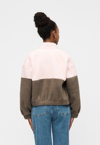 Φλις πουλόβερ με ψηλό γιακά, που διαθέτει ροζ και καφέ πάνελ. Χαλαρή εφαρμογή με ελαστικά μανίκια και υφή μαλακή και ανάγλυφη.