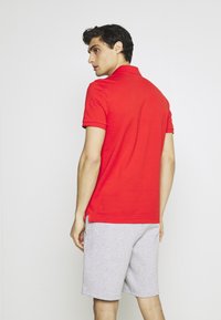 Rode polo met korte mouwen en een kraag, gecombineerd met lichtgrijze sportshorts. Soepele katoentextuur, met zijsplitten aan de zoom.