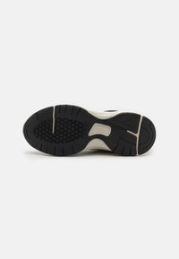 Sottopiede delle sneakers con una superficie in gomma nera testurizzata, caratterizzata da un motivo esagonale, una suola intermedia bianca e scanalature evidenti per la presa.