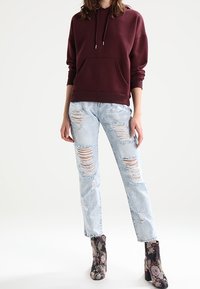 Sudadera con capucha burdeos, bolsillo delantero, combinada con jeans rotos de color azul claro y botines estampados con acentos florales.