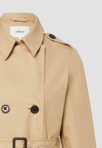Beiger Trenchcoat mit spitzem Kragen, schwarzen Knöpfen, Schulterklappe und passendem Gürtel, gekennzeichnet mit s.Oliver Größe 36.