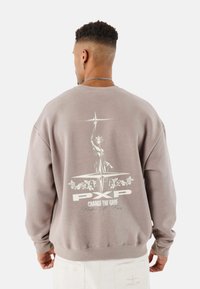 Sudadera gris con hombros caídos y cuello redondo. Presenta una impresión gráfica de una estatua y texto en la parte posterior. Material suave, ajuste casual.
