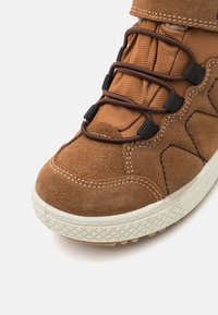 Brune semskede sneakers med teksturert stoff, elastiske snører og en hvit gummisåle med mønstredd grep for godt feste.