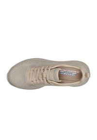 Scarpa sportiva beige con tomaia in maglia testurizzata, chiusura a lacci e suola imbottita. Presenta un logo sulla soletta e un'asola sul tallone.