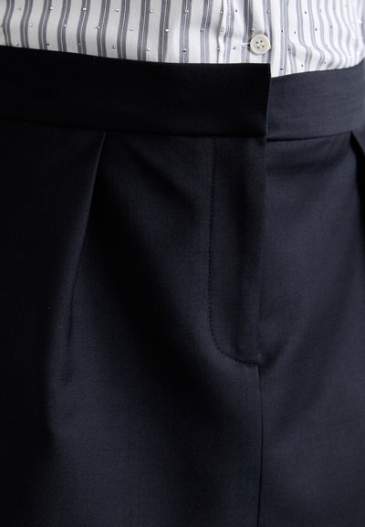 Pantaloni de costume navy cu o textură netedă, având un design plisat, buzunar lateral unic și un brâu plat. Detaliu cu nasture în partea de sus.