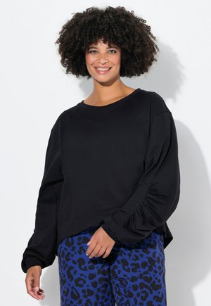Sudadera negra de manga larga con un corte holgado y mangas fruncidas, combinada con pantalones con estampado de leopardo azul. Textura suave.