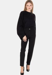 Top nero a maniche lunghe con vestibilità ampia e maniche larghe, abbinato a pantaloni neri sartoriali con passante per cinta e un semplice dettaglio argentato.