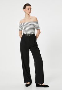En off-the-shoulder top med striber i hvid og sort, parret med højtaljede sorte bukser, der er spændt ind med et rundt sølvspænde, samt sorte flade sko.