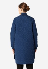 Dlouhý šedý prošívaný kabát s diamantovým vzorem, žebrované manžety a vysoký límec, navržený pro izolaci a pohodlí.