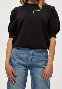 Černý top s balónovými rukávy vyrobený z jemné tkaniny, který má kulatý výstřih. Spárovaný se světle modrými džíny s vysokým pasem a volnějším střihem.