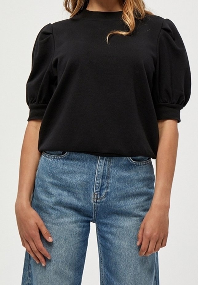 Černý top s balónovými rukávy vyrobený z jemné tkaniny, který má kulatý výstřih. Spárovaný se světle modrými džíny s vysokým pasem a volnějším střihem.
