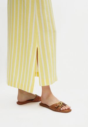 Sandalias planas marrones con hebilla dorada, combinadas con un vestido amarillo de rayas, de largo hasta el tobillo, con una abertura frontal y un acabado en el dobladillo.