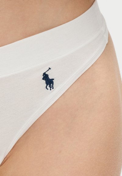 Κοντινή λήψη ζωνάρι λευκού εσώρουχου με κεντημένο λογότυπο παίκτη πόλο σε μπλε ναυτικό χρώμα πάνω σε γυμνό δέρμα.