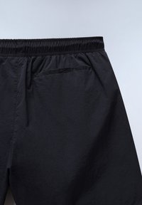 Zwarte shorts met elastische taille en een achterzak aan de rechterkant, gemaakt van lichtgewicht, licht gestructureerde stof op een effen lichte achtergrond.