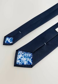 Marinefarbener strukturiertem Krawatte mit gemustertem hellblauem Innenfutter, das ein florales Design und spitz zulaufende Enden aufweist, gesichert mit sichtbaren Nähdetails.