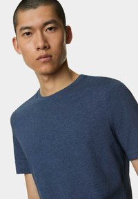 Námořnická modrá tričko s kulatým výstřihem vyrobené z měkké, strukturované tkaniny. Má krátké rukávy a volný střih. Bez viditelných log nebo vzorů.