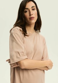 Jasny beżowy t-shirt z krótkim rękawem wykonany z miękkiej bawełny, z okrągłym dekoltem i luźnym krojem. Gładka tekstura z minimalnymi detalami szycia.