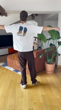 Bijela majica s grafikom Timberland čizama, smešane uzorkovane hlače i bijele tenisice. Unutrašnji prostor s biljkama i kaučem.