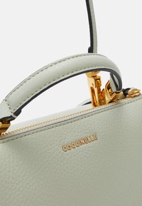 Vaaleanvihreä nahkalaukku, jossa on jämäkkä muoto, kultaiset yksityiskohdat, vetoketjukiinnitys ja ylhäällä oleva kahva, jossa on erottuva ompelu.