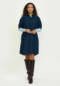 A haditengerészeti ruha rövid puffos ujjakkal, gombos elülső résszel és redős részletekkel, valamint kerekített aljúval rendelkezik, melyet barna térdig érő csizmával párosítottak.