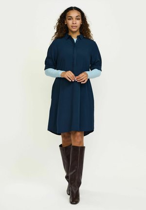 A haditengerészeti ruha rövid puffos ujjakkal, gombos elülső résszel és redős részletekkel, valamint kerekített aljúval rendelkezik, melyet barna térdig érő csizmával párosítottak.