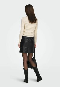 Haut à manches longues crème côtelé associé à une mini-jupé en cuir noir. Bottes de cowboy noires montantes jusqu'aux genoux et sac à bandoulière noir complètent le look.