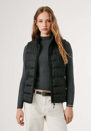 Chaleco acolchado negro con cuello alto, cierre de cremallera, diseño acolchado y material ligero, que se lleva sobre un suéter de canalé gris.
