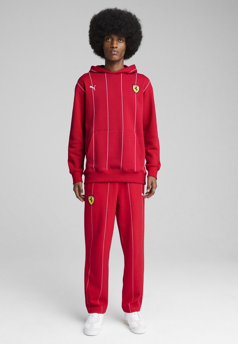 Rød hættepullover med hvide striber, kængurulomme og Ferrari-logo; parret med matchende røde sweatpants med logo og hvide striber.