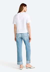 T-shirt blanc à manches courtes avec un logo discret à l'arrière, associé à un jean droit bleu clair avec des revers et des bords légèrement effilochés.