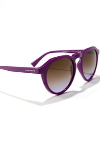 Violetinės plastikinės saulės akiniai su rudos spalvos gradientinėmis lęšiais, kampuotu dizainu ir metaliniu logotipu šone. Blizgus paviršius ir plačios rėmeliai.