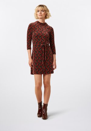 Vestido rojo de estampado con mangas tres cuartos, cintura con lazo y una textura suave. Llevado con botas de tobillo marrones brillantes.