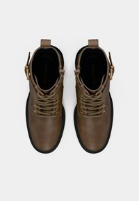 Καφέ δερμάτινα μποτάκια μέχρι τον αστράγαλο με στρογγυλή μύτη, επίπεδη καουτσούκ σόλα και μεταλλικές λεπτομέρειες. Διαθέτουν κορδόνια και λουρί με λεπτομέρεια αγκράφας.