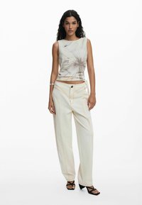 Top senza maniche di colore chiaro con motivo astratto, abbinato a pantaloni palazzo crema con cuciture arancioni e chiusura anteriore con bottone.
