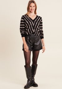 Schwarz-beige gestreifter Pullover mit V-Ausschnitt, kombiniert mit schwarzen Leder-Shorts und kniehohen schwarzen Boots. Silberner Schmuck als Akzent.