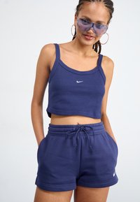 Tamsiai mėlynas ovenukinis braletė su plonomis petnešėlėmis, puošia mažas baltas Nike logotipas. Pora su atitinkamais tamsiai mėlynais trumpais šortais su raišteliu, medžiaga yra lygi ir minkšta.