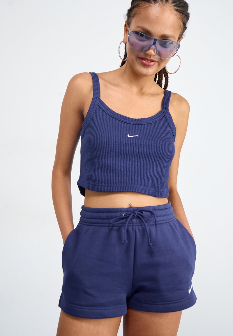 Top court côtelé en marine avec des bretelles fines, arborant un petit logo Nike blanc. Assorti à un short bleu marine à cordon de serrage, le tissu est lisse et doux.