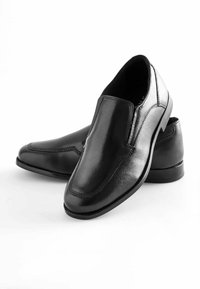 Schwarze Lederlofer mit glatter Oberfläche, dekorativer Naht und leicht elongated Form, auf einem niedrigen Absatz.