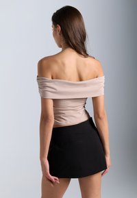 Beige Carmen-Bluse mit weicher, glatter Textur, kombiniert mit einem schwarzen Minirock in schlichter Ausführung und zwei Gesäßtaschen.