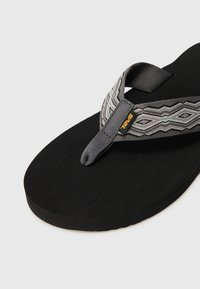 Svart flip-flop med en teksturert såle, med en gråmønstret stropp med geometriske design og et lite oransje logomerke.