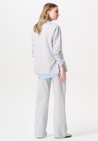Helles graues sweatshirt mit langen Ärmeln, das über einem hellblauen kragenhemden getragen wird, kombiniert mit passenden grauen weiten Hosen. Weicher Stoff, lockere Passform.