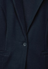 Mörk marinblå blazer med en slät yta, skarpa slag och två framfickor. Den har en enkel knapplist med en fyrhålsdesign.