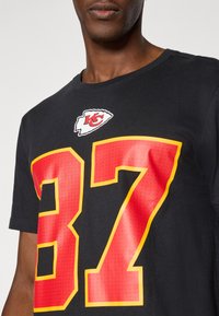 Sort kortærmet t-shirt med et stort rødt nummer 87 omrids i gult, med et Chiefs-logo ovenfor i hvid og rød. Glat tekstur.