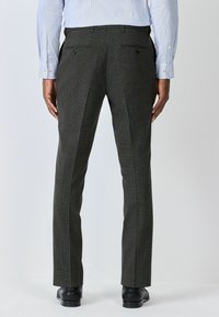 Graue gemusterte Hose mit maßgeschneidertem Schnitt, ausgestattet mit Gesäßtaschen, Seitennähten und einer glatten Textur. Kombiniert mit schwarzen Schuhen.