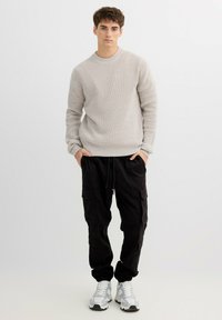 Suéter gris claro acanalado con cuello redondo, combinado con pantalones cargo negros con bolsillos laterales, complementados con zapatillas grises.