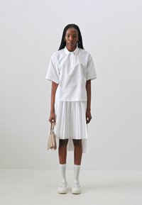 Hvitt bomullsblandingsantrekk med krage, kortermet topp og plisserte skjørt, kombinert med hvite sneakers og en liten beige veske.